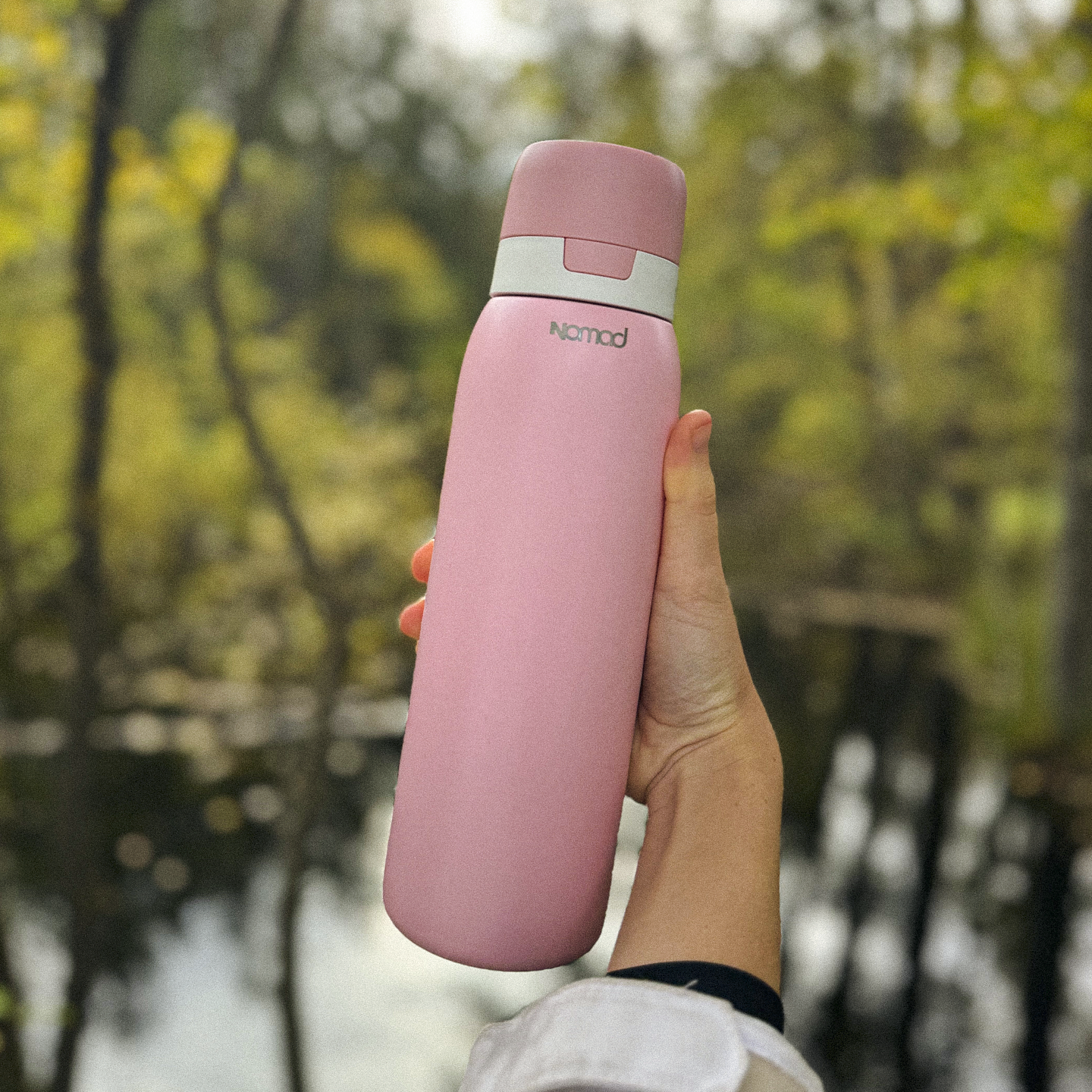 NOMAD Pink water bottle SafeSip filtration bottle held in a hand with a blurred natural background