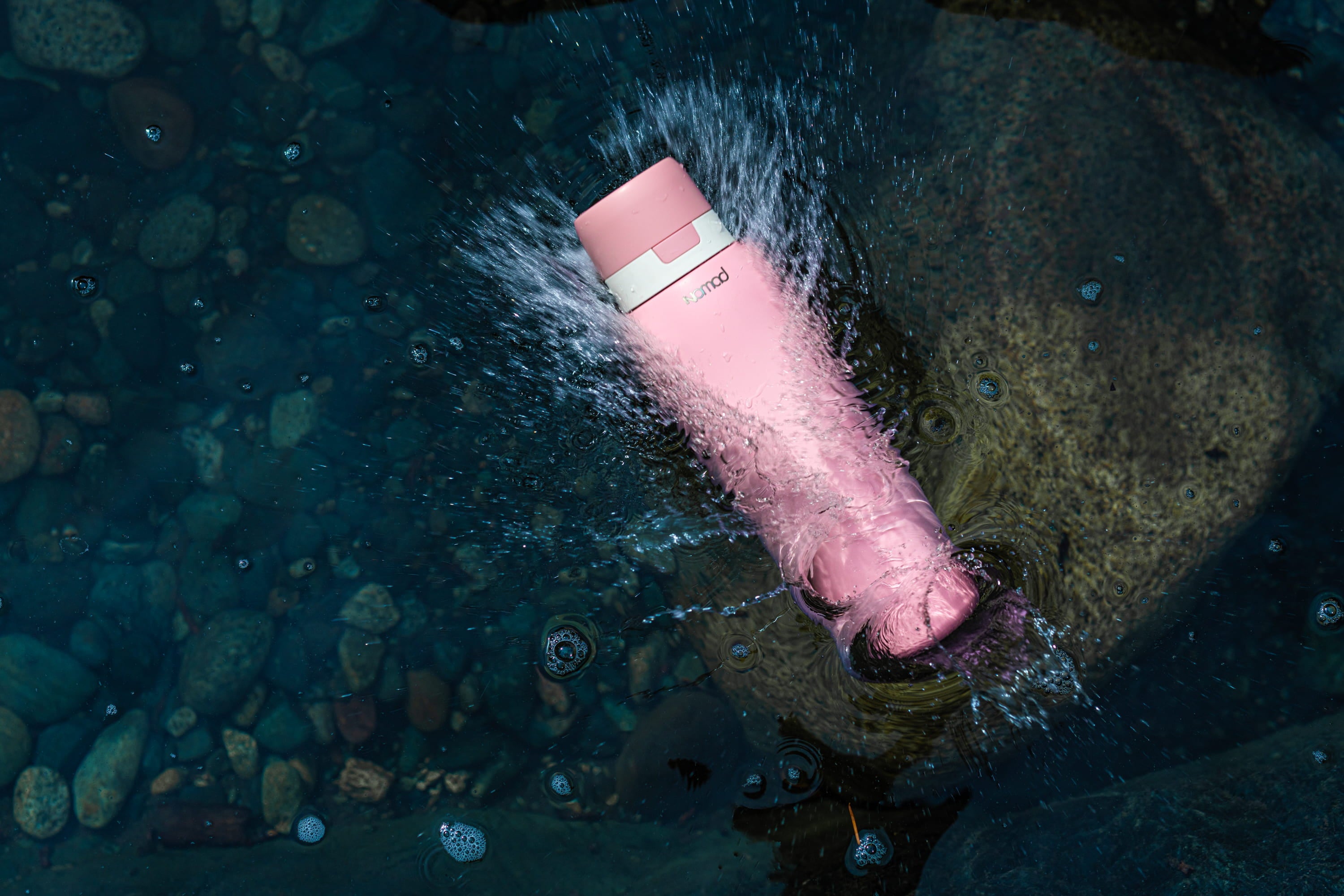 Himalayan Pink NOMAD SafeSip purifier bottle surrounded by splashing water in a clear rocky mountain stream