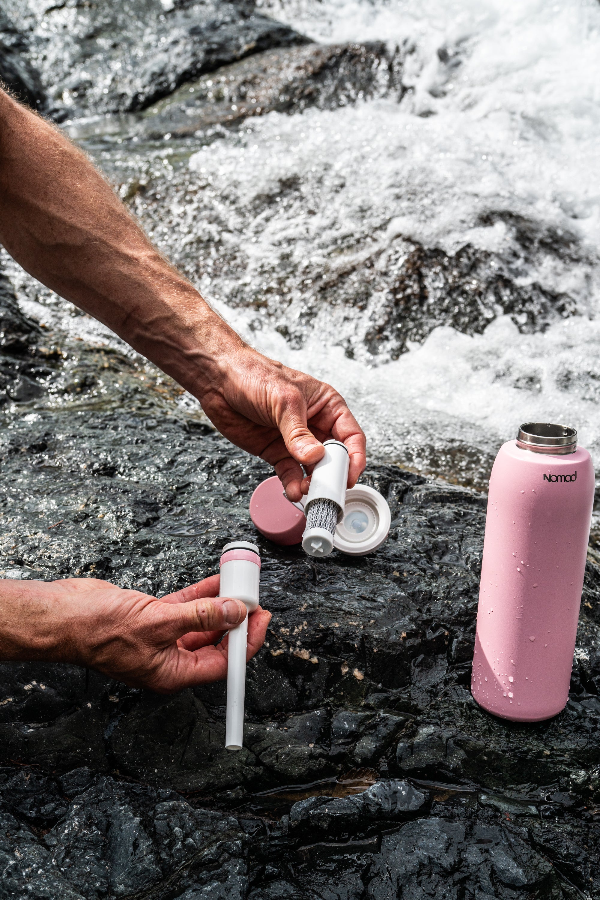 A person's hands are shown how to assemble the water filter cartridge outdoors into the NOMAD SafeSip purifier and insulated water bottle