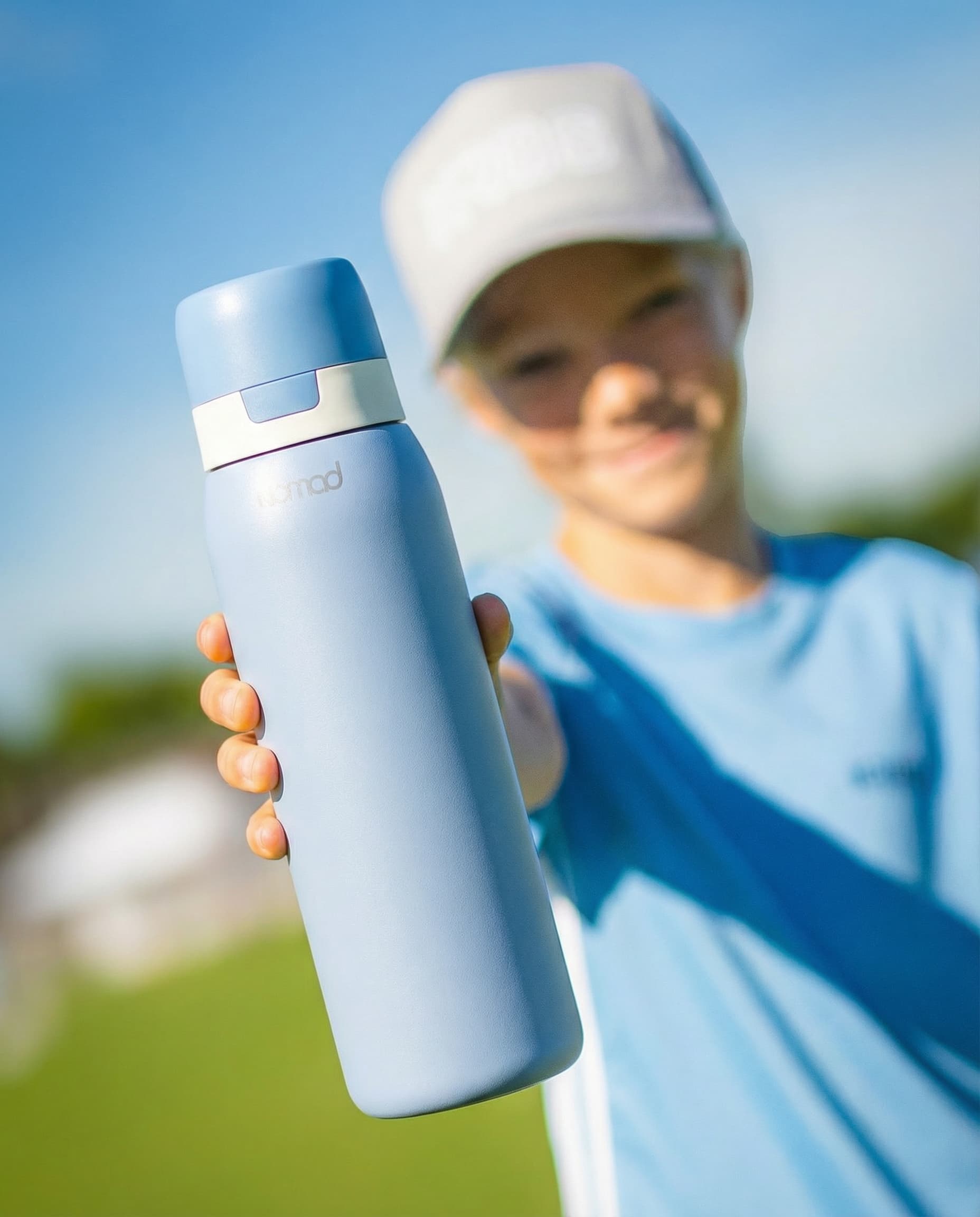 Close-up of a light blue NOMAD reusable water bottle held outdoors