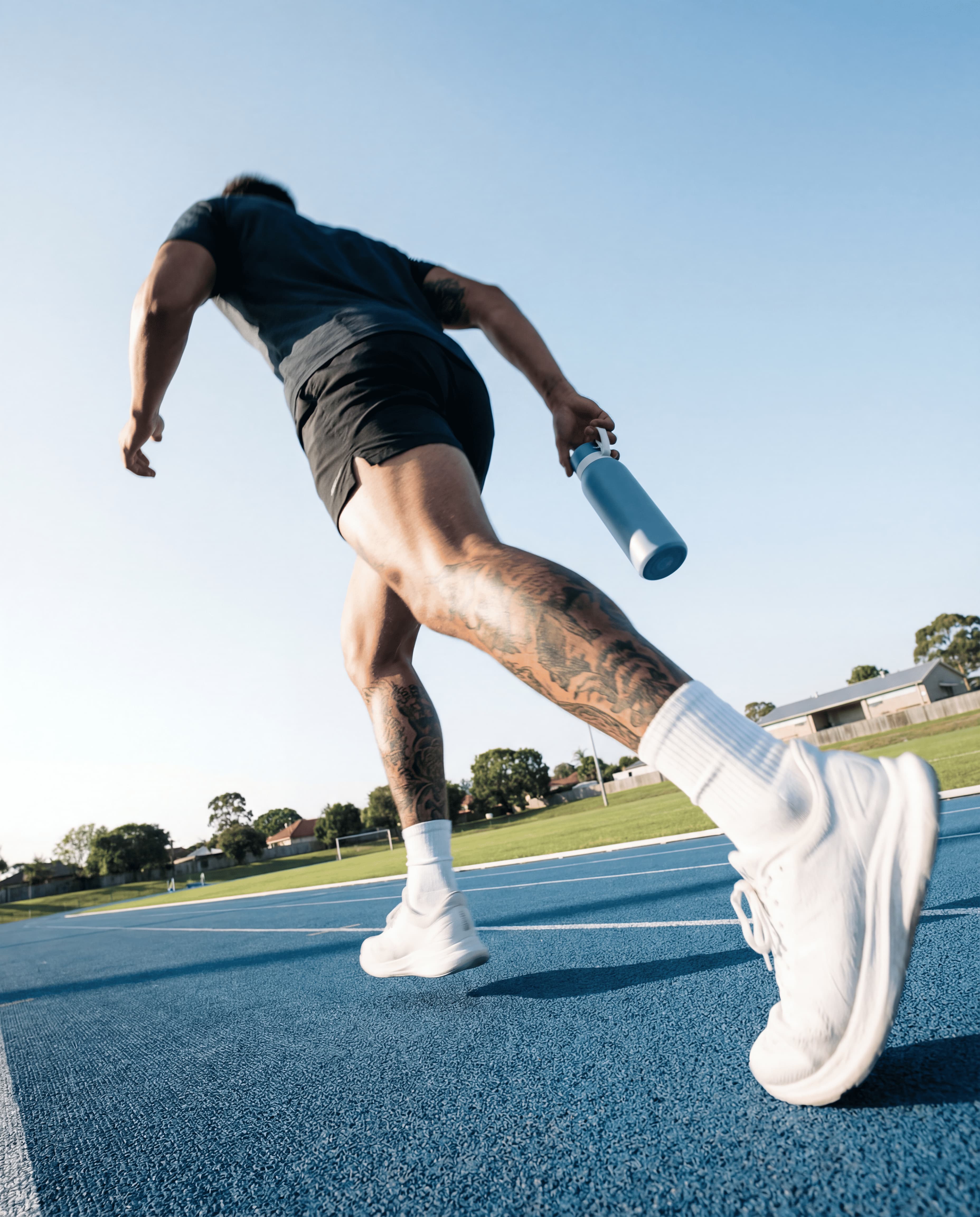Man sprinting on an outdoor track holding a light blue NOMAD reusable water bottle