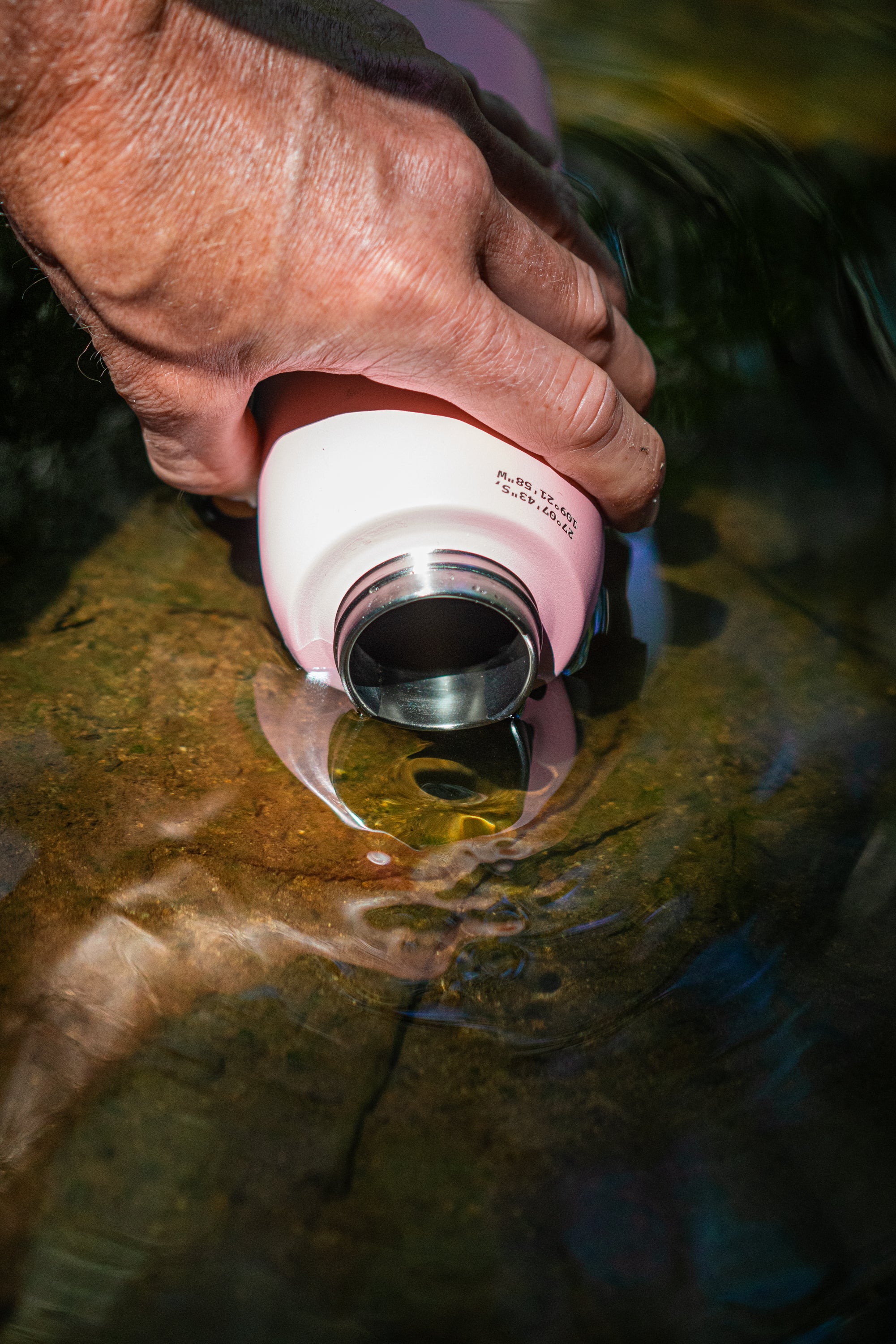 Close-up of a NOMAD SafeSip water filter bottle being filled from a remote mountain lake