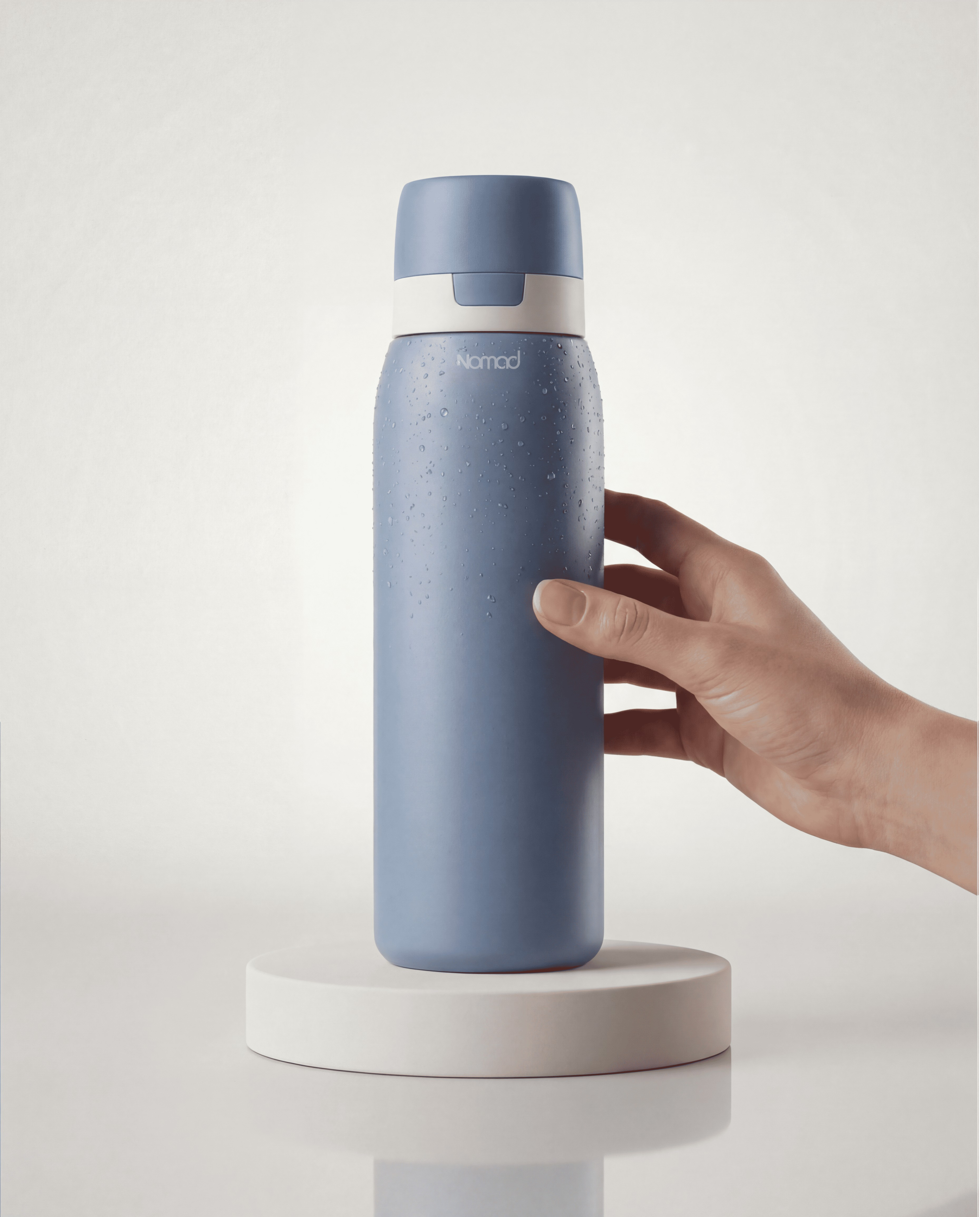 NOMAD Blue bottle studio light and white background with a women hand touching the filtered water bottle. Dynamic product photoshoot