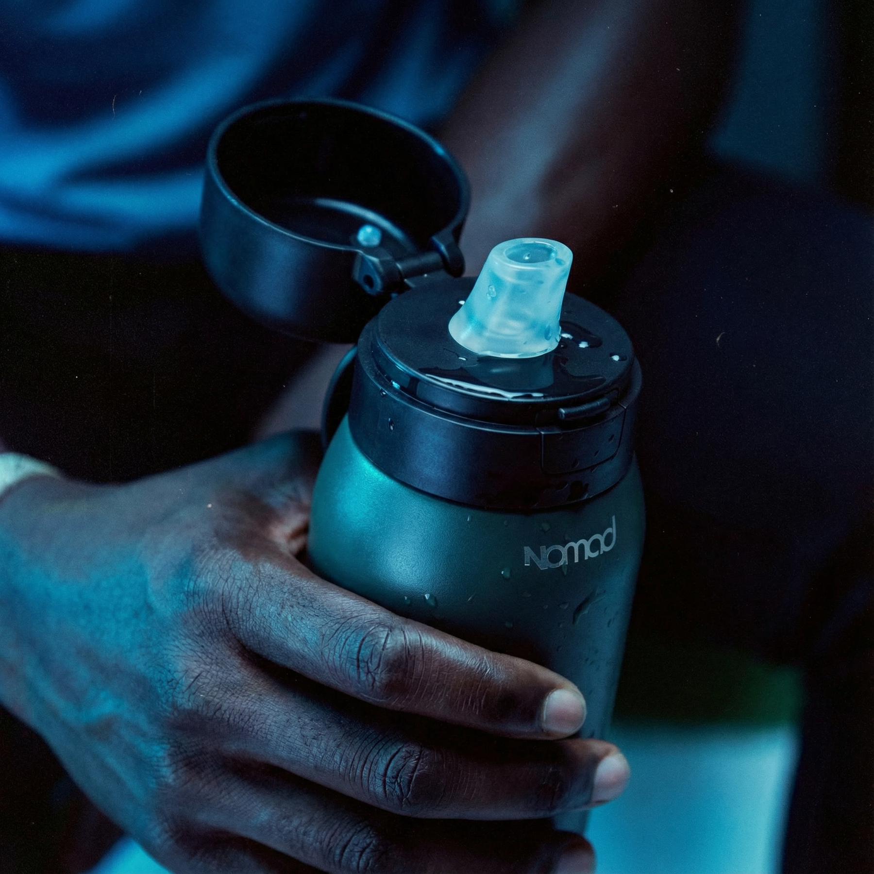 Person holding a nomad filtered black water bottle with a blue light on a dark background #color_midnight-green