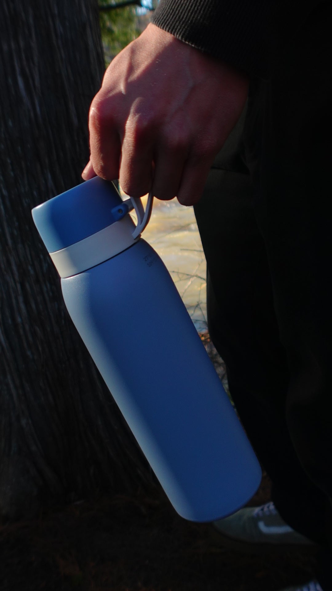 Someone holding the SafeSip Blue Azure in the woods.