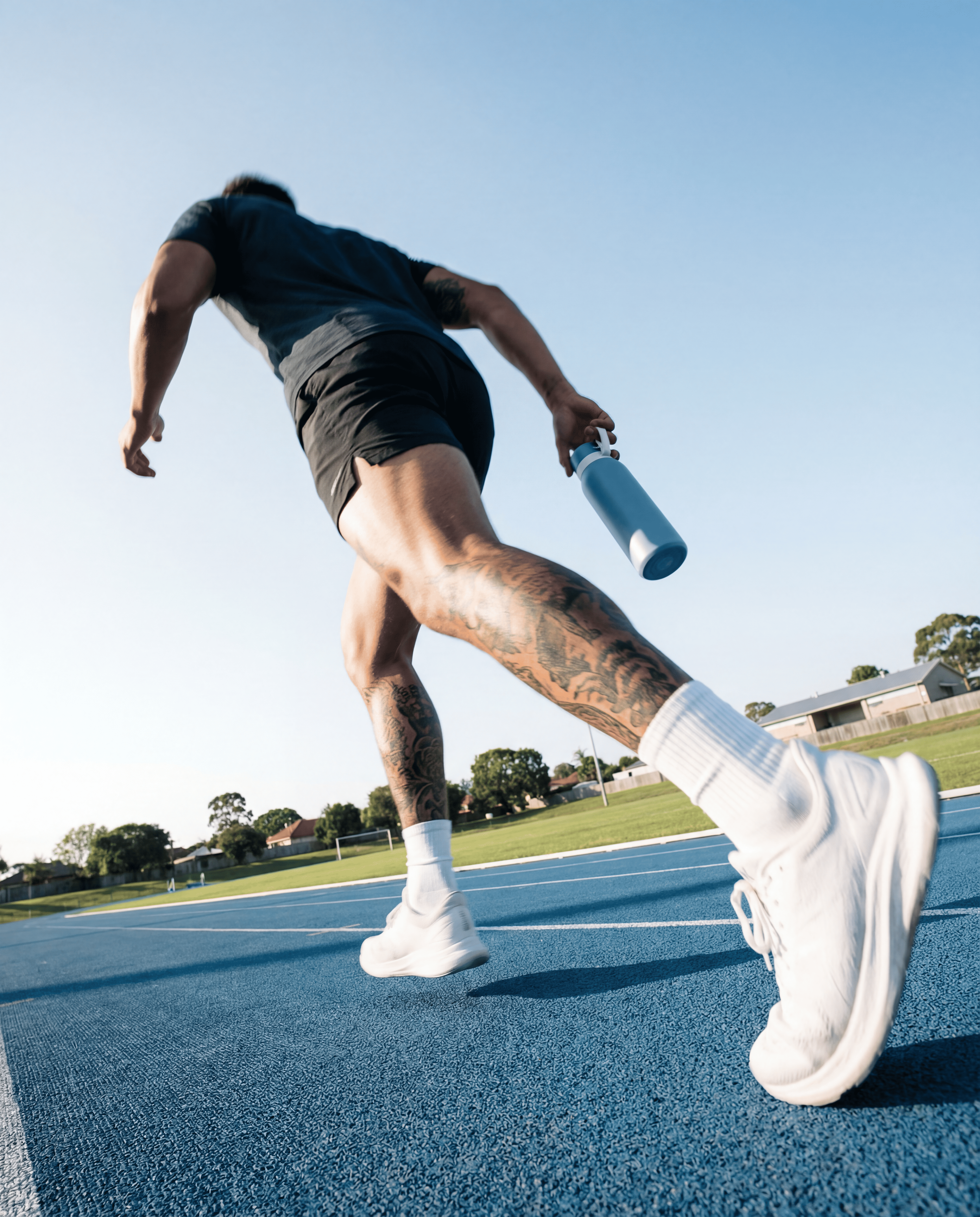 Person running on a track with a blue NOMAD Bottle with a blue sky and green field in the background