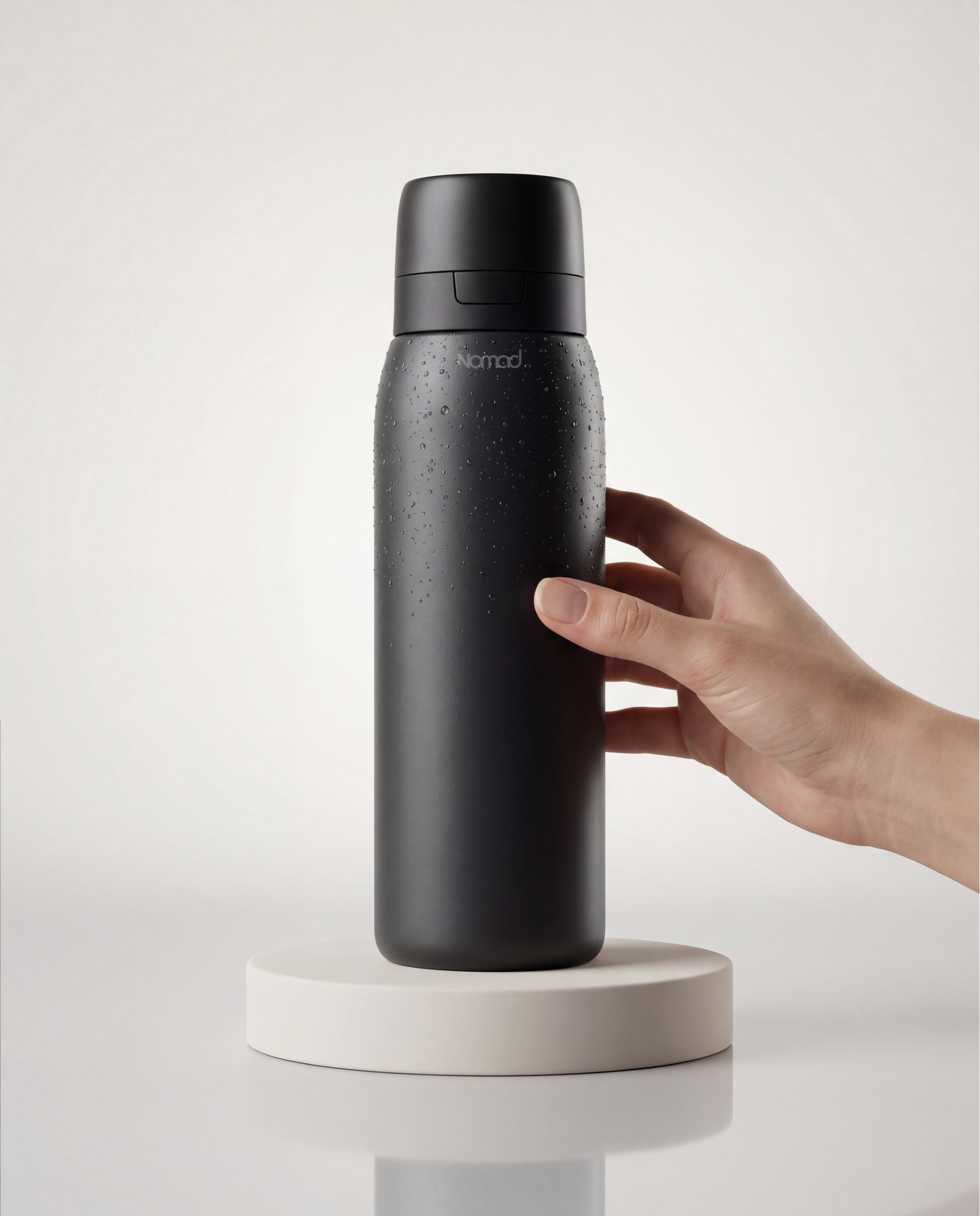 NOMAD SafeSip Black filtered water bottle held by a hand on a white background