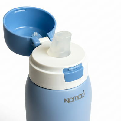 NOMAD SafeSip Blue water bottle with a white cap and blue lid on a pure white surface. 