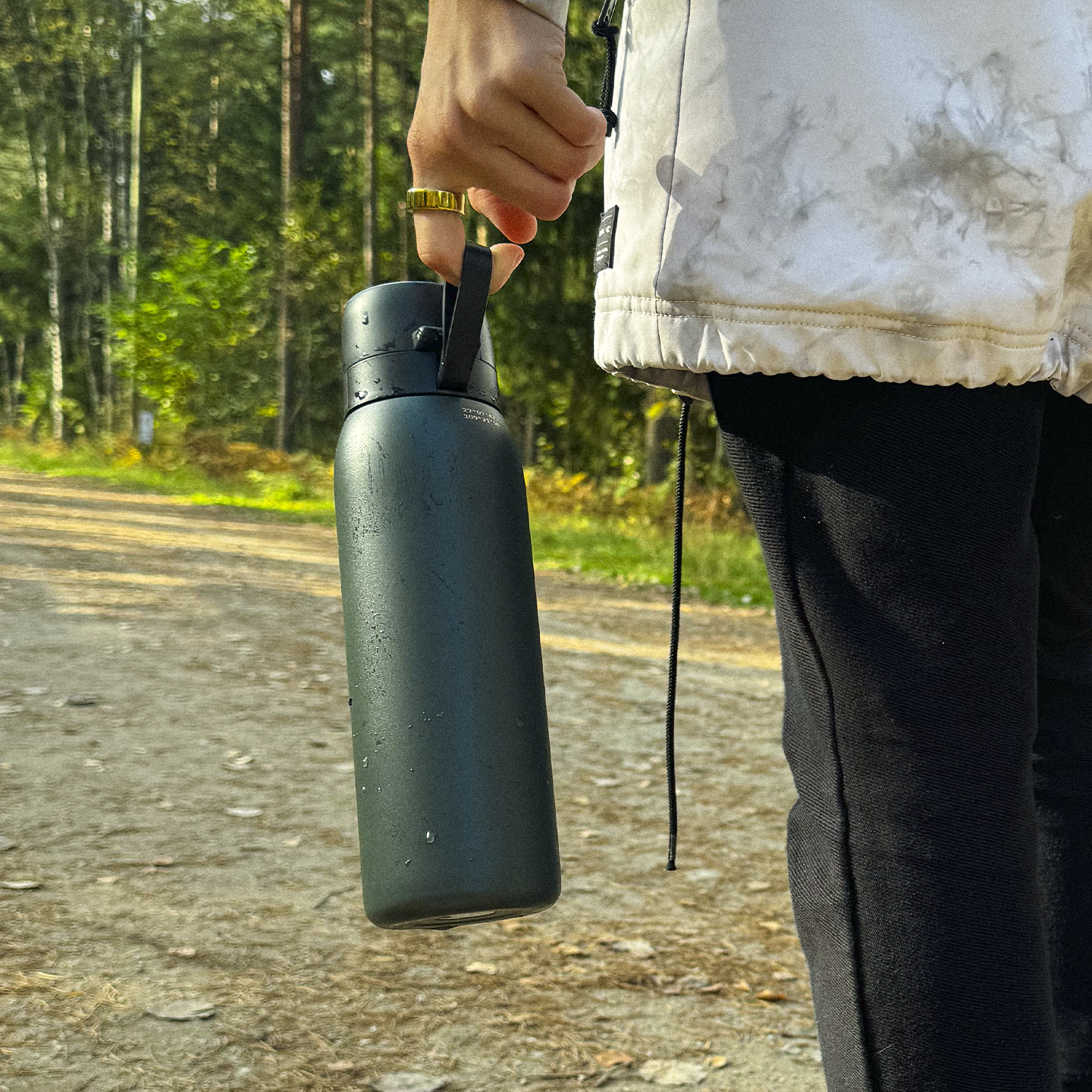 Person holding a black Safesip water bottle made for outdoors, with trees in the background