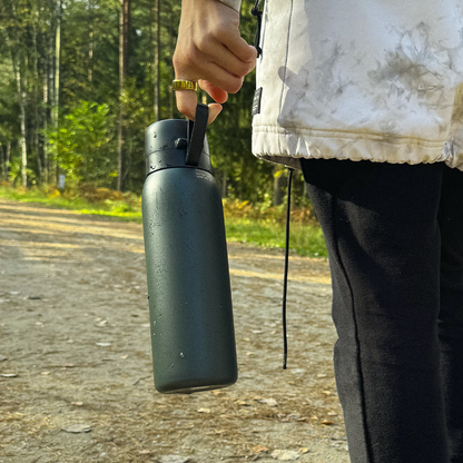 Person holding a black Safesip water bottle made for outdoors, with trees in the background
