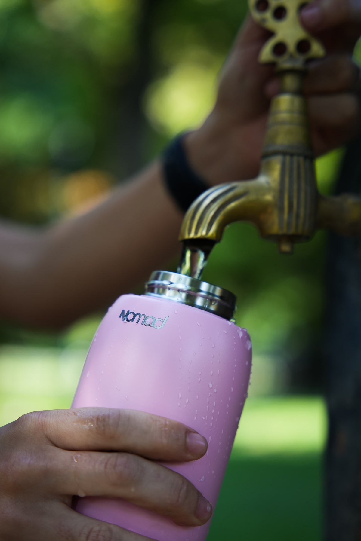 Pink NOMAD SafeSip water purifier bottle being filled from an outdoor drinking water tap for clean and sustainable water anywhere you go.