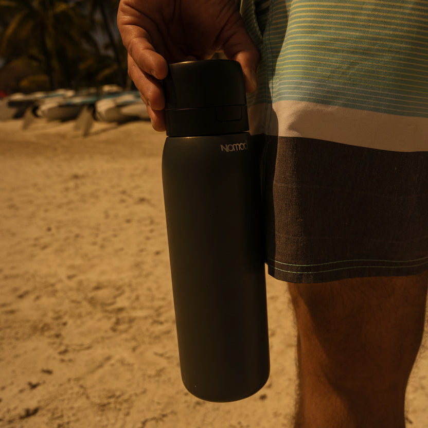 Person holding a black Filtered SafeSip bottle with a beach in the background