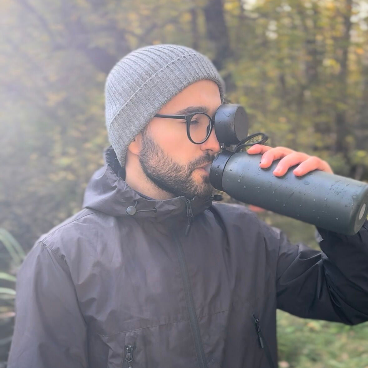Man drinking from a thermos SafeSip Bottle outdoors in a forest.