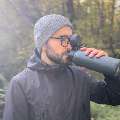 Man drinking from a thermos SafeSip Bottle outdoors in a forest.