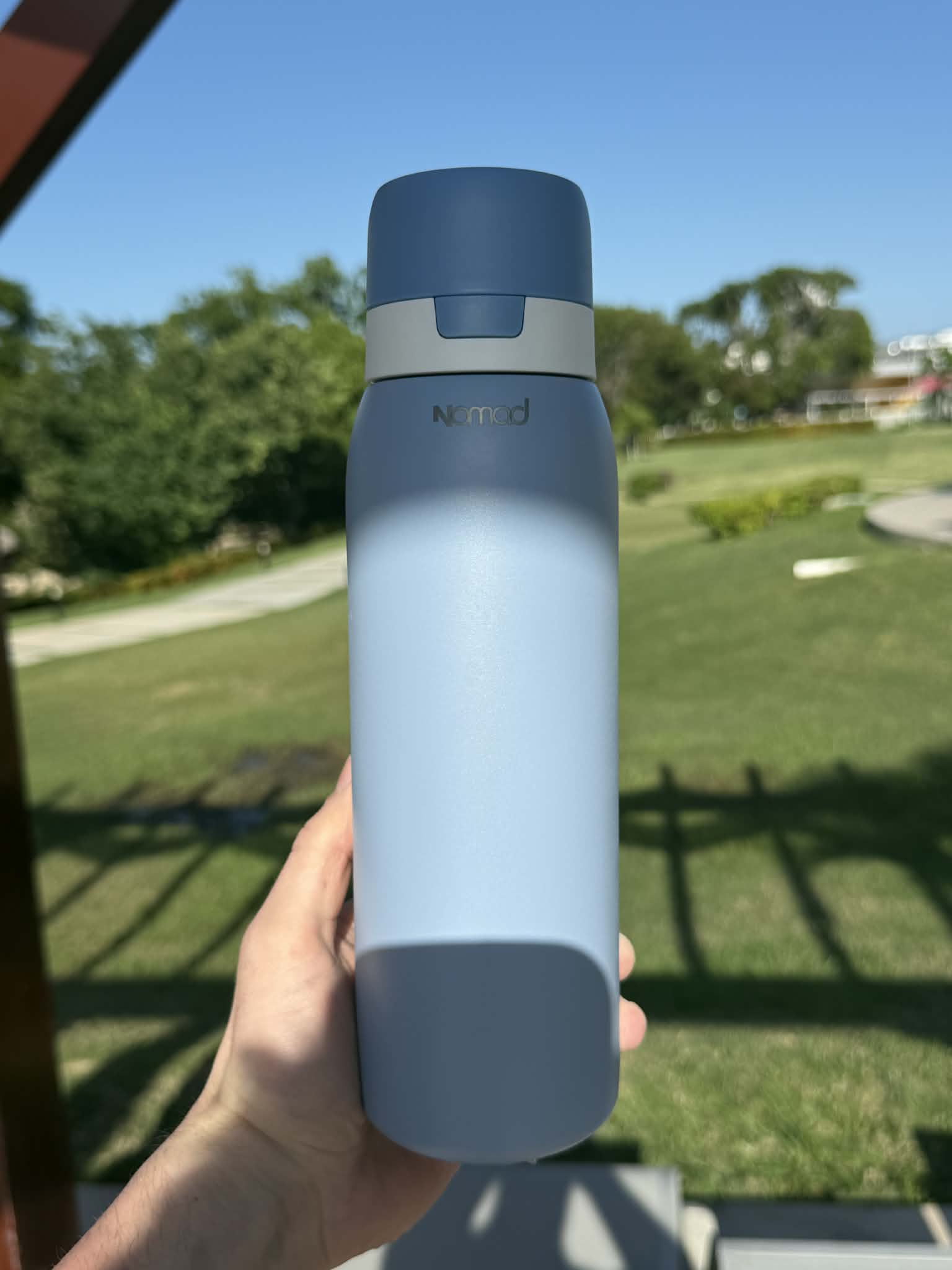 Person holding a blue safesip water bottle with a park in the background