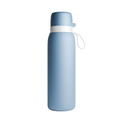 A matte light NOMAD SafeSip blue insulated water bottle with a white collar and a white carrying loop, shown on a plain white background. 