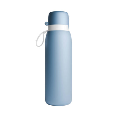 A matte light blue NOMAD SafeSip insulated purifier water bottle with a matching blue cap, a white band around the neck, and a small white carrying loop, shown on a plain white background. 