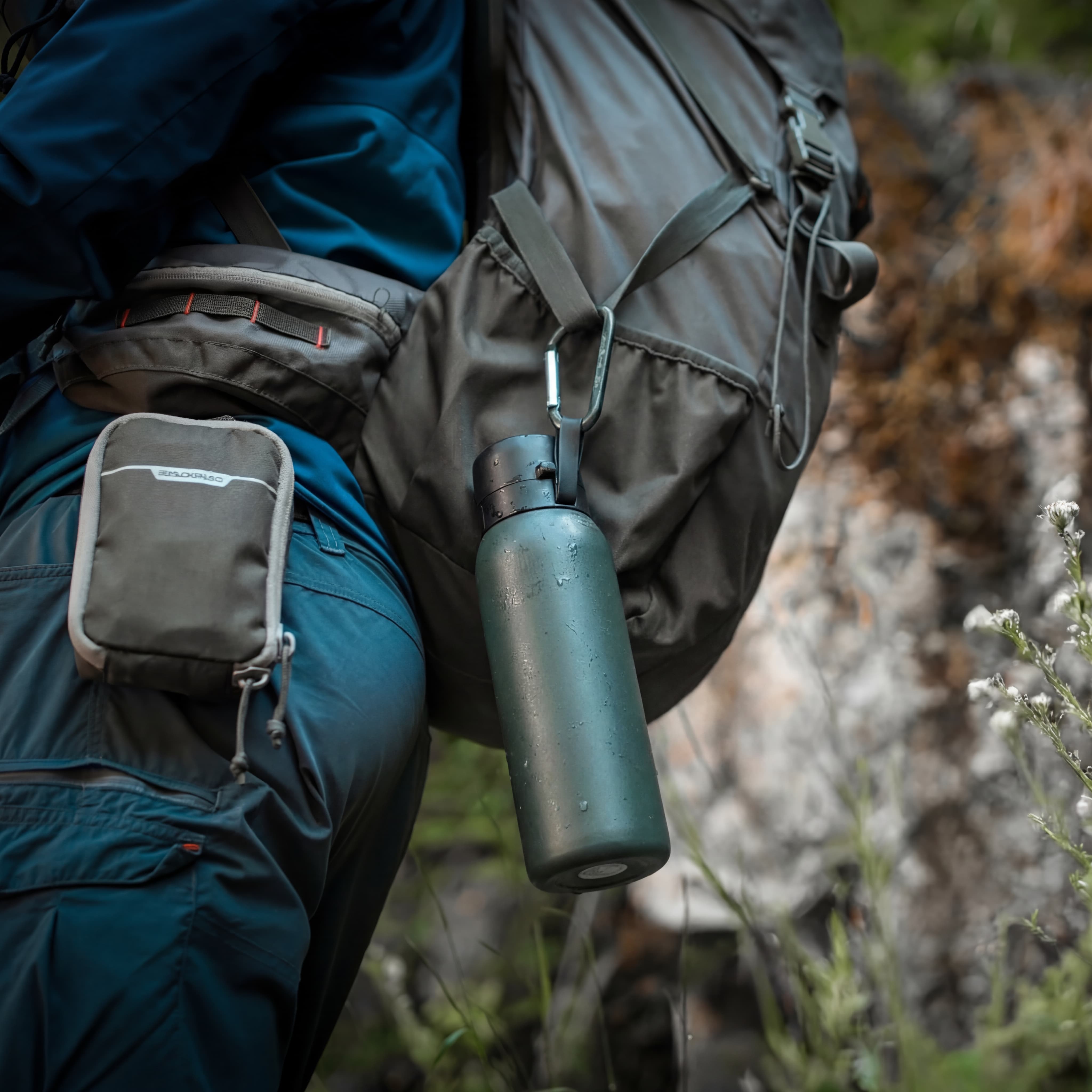 Person wearing a backpack with a NOMAD green forest water bottle and pouch in a natural setting