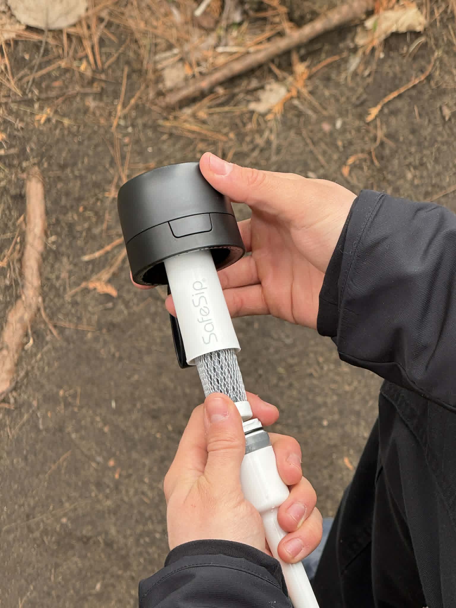 Person holding a SafeSip Purifier Bottle with the advanced cartridge inside against a natural background.