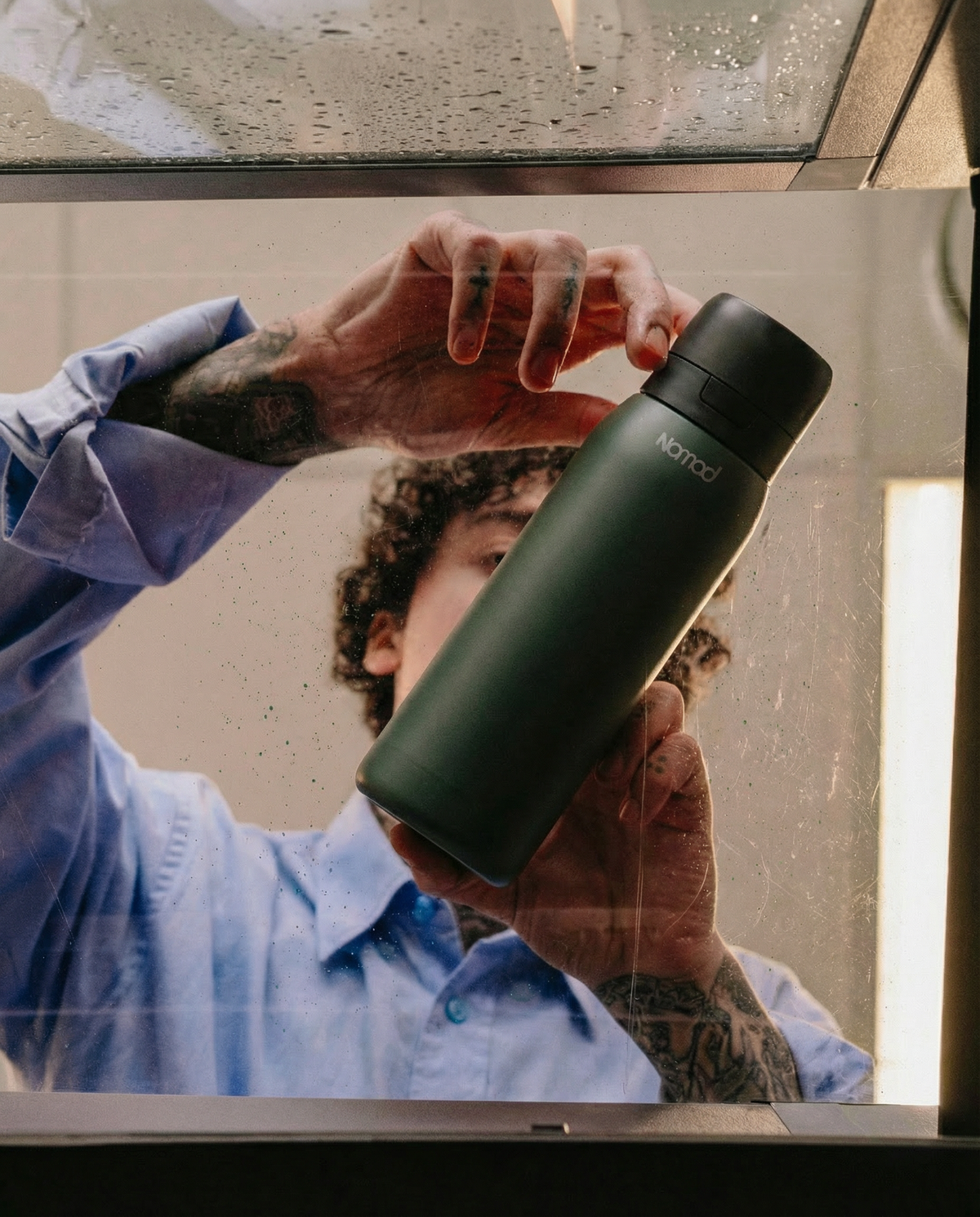 Person holding a Nomad Safesip green water bottle with a blurred background