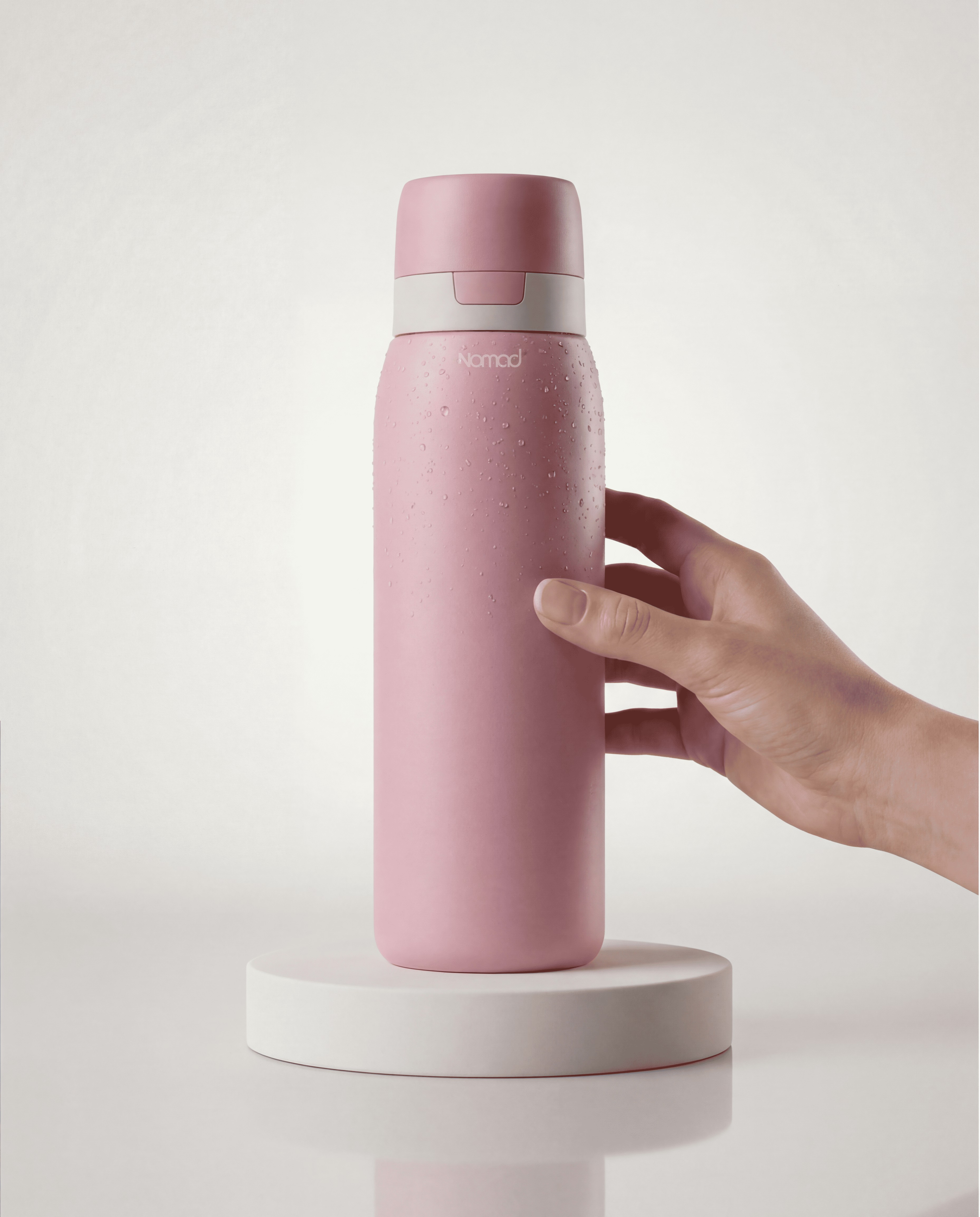 Filter your tap or natural water using NOMAD SafeSip. Picture on white background with a hand grabing the bottle.